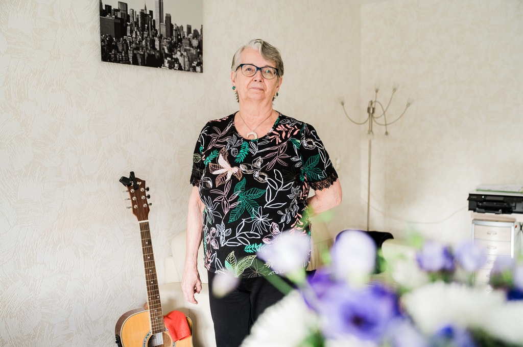Mevrouw Weeda staand in appartement naast gitaar