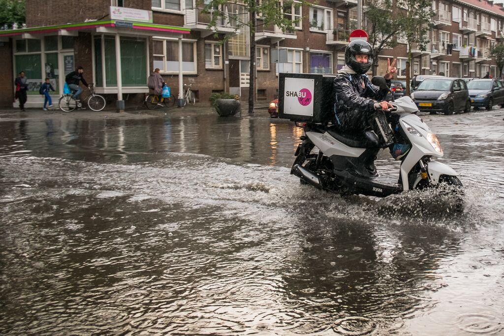 Bezorger op scooter rijdt door water op straat