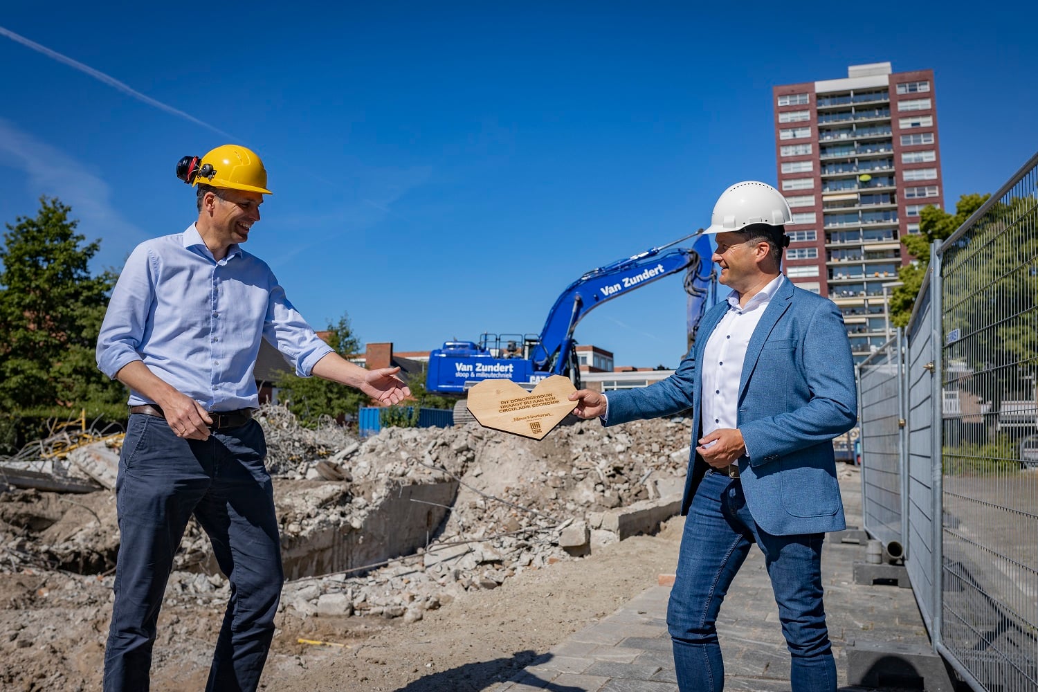 Alexander overhandigt houten hart aan Alex op de bouwplaats