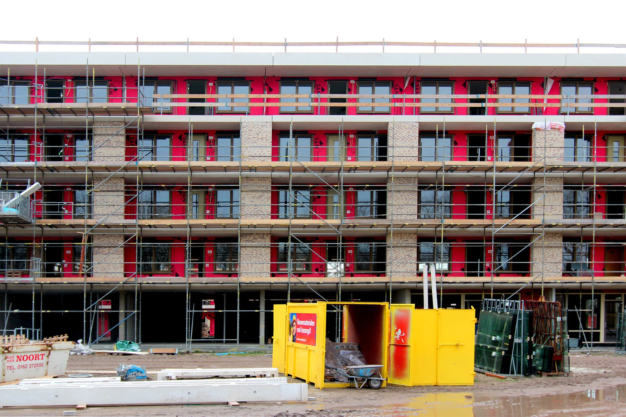 De achterkant van gebouw in aanbouw met de steigers en een container voor het gebouw