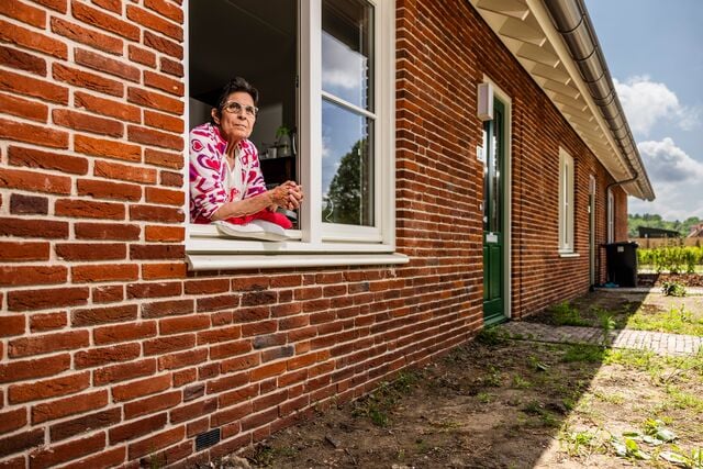 Bewoner kijkt uit het raam van haar woning
