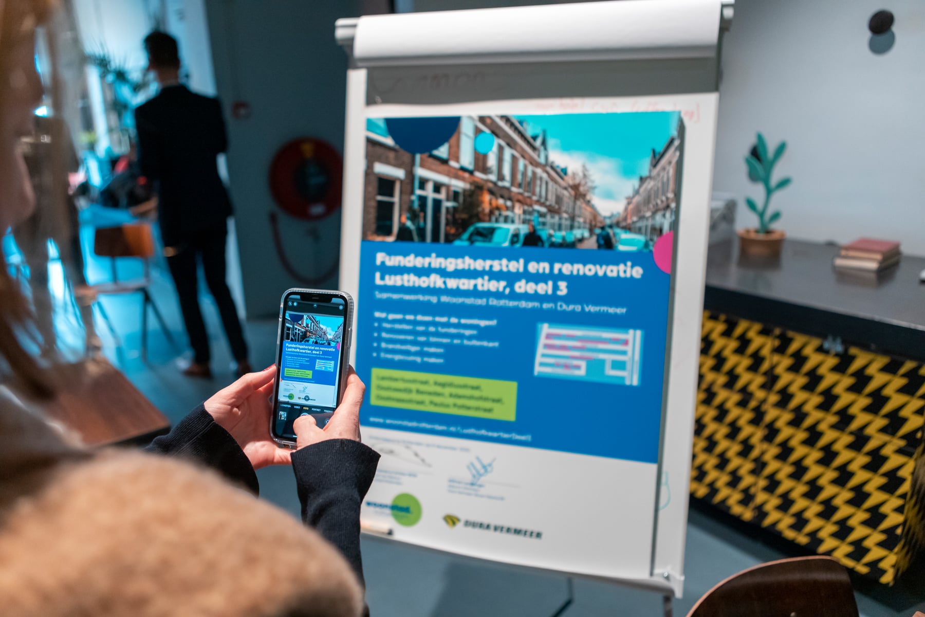 Iemand maakt met een telefoon een foto van het renovatiebord Lusthofkwartier