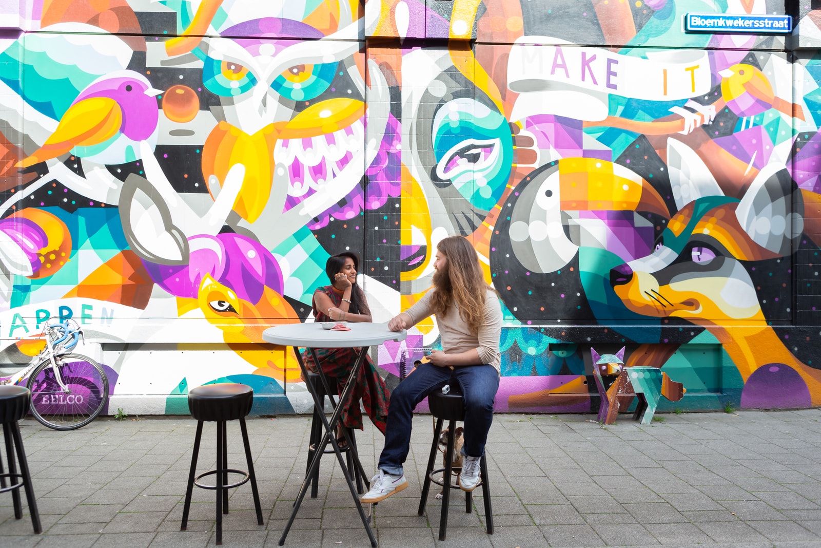 Parricia en Maxim zittend aan een tafeltje voor een street art muur