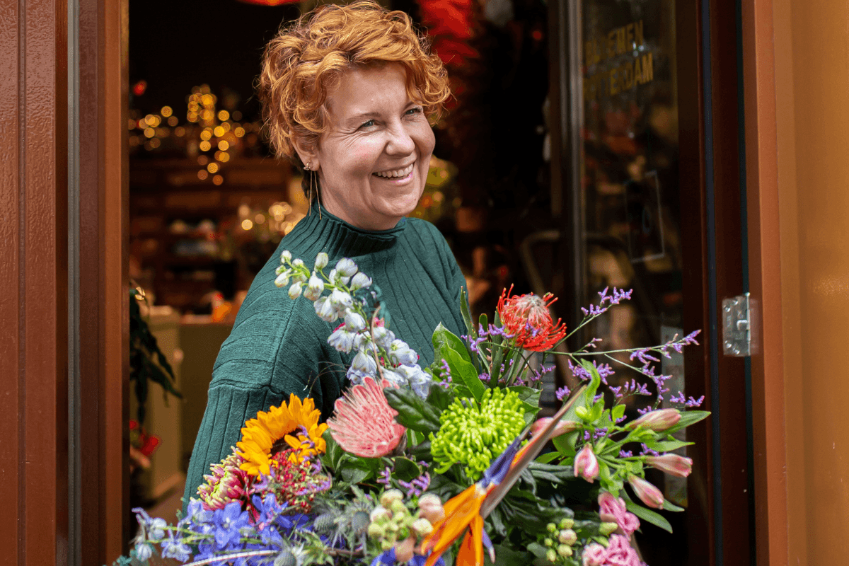 Elvira Hoogerwerf lachend in deuropening met bos bloemen