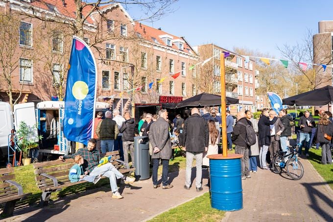 Feest aan de Bellamystraat waar mensen bij elkaar staan, tussen kraampjes met eten