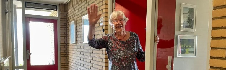 Ada Straatsma zwaaiend in de deuropening van Thuisplusflat