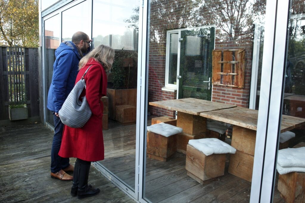 Serge en Caroline kijken door ruit woning naar binnen